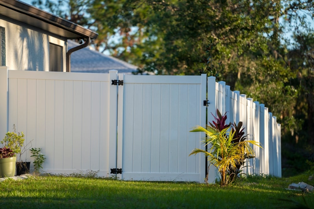 White vinyl fence on a green lawn providing backyard security and privacy, an example of the durable options offered by landscape services in Slidell.
